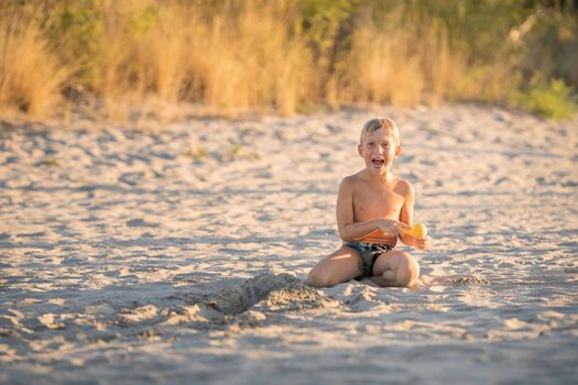 Little blond boy playing with small colorful plastic sand toy on the beach, kid building a sandcastle with fun, active happy summer holiday.