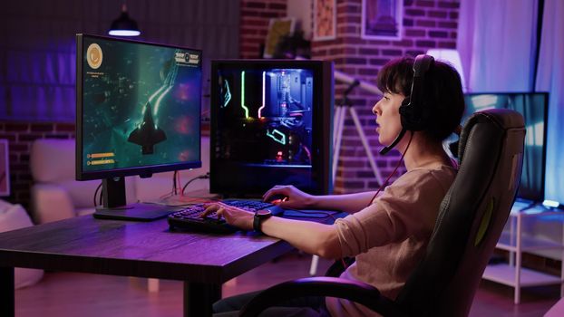 Woman relaxing and streaming on internet fast paced space shooter simulation gameplay while talking using headset. Gamer girl playing rpg action game on professional pc setup in living room.