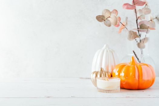 Details of Still life, pumpkins, candle, brunch with leaves on white table background, home decor in a cozy house. Autumn weekend concept. Fallen leaves and home decoration