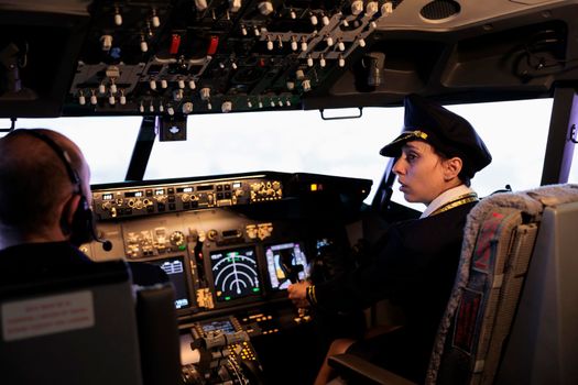 Woman copilot in uniform flying airplane with cockpit command buttons on cabin dashboard. Pushing engine and radar switch on control panel board to fly jet with traffic navigation.