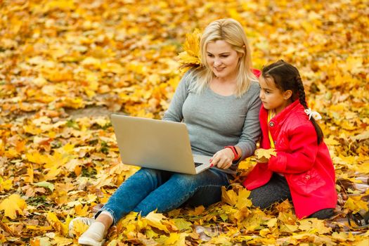 Happy mother and her tdaughter using laptop in the park