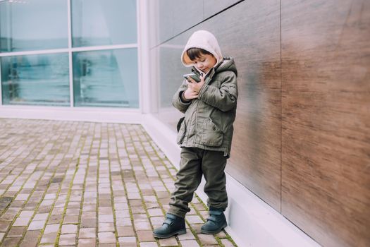 A boy looks at his phone in the city of lifestyle . Modern technologies. Modern children. A child and a phone. Urban lifestyle