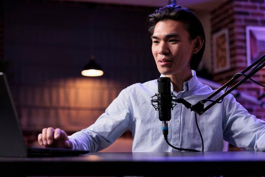Asian man broadcasting online podcast show on vlogging channel, recording video at radio sound station. Livestreaming vlog and filming with audio equipment production on social media.