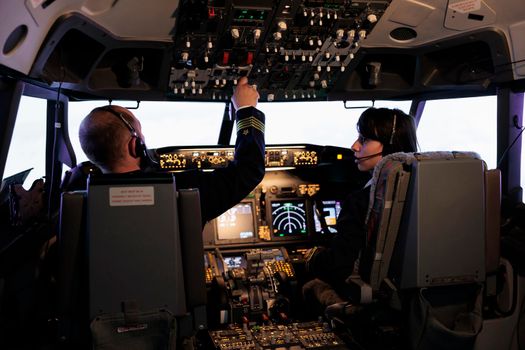 Captain and copilot using dashboard command to takeoff with plane, flying aircraft with control panel switch and buttons. Radar handle in aircrew cabin to fly airplane with windscreen.