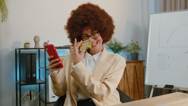 Businesswoman programmer software developer working, making online purchase payment shopping with credit bank card and smartphone at modern office desk with laptop. Female freelancer business woman