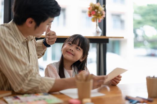 Happy proud asian father and daughter having fun together, drawing and painting watercolor