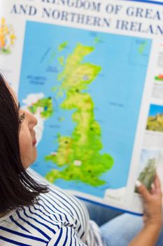 Woman looks at poster map of England, English teacher with educational training material on foreign language, top view, vertical image