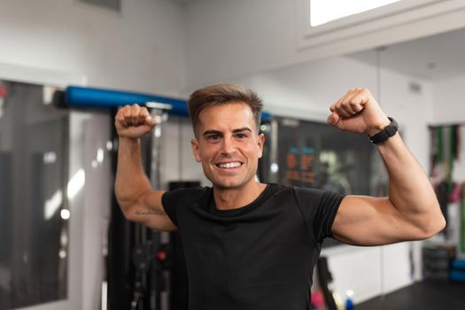 A male coach showing off her muscles with her arms raised as a symbol of victory at the gym