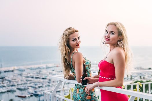 pretty young girls with beers posing and having fun at a private party on the outdoor terrace in front of the port, leisure happiness and friendship concept, copy space for text