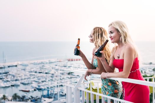 beautiful young girls drinking beers and having fun at a private party on the outdoor terrace in front of the port, leisure happiness and friendship concept, copy space for text
