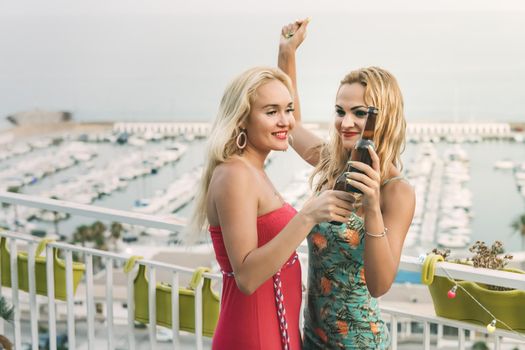 carefree young girls with beers dancing and having fun at a private party on the outdoor terrace, leisure happiness and friendship concept