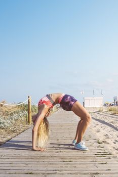 female athlete stretching and doing yoga exercises, sporty blonde girl doing warm up workout at promenade before training and running, fitness and healthy lifestyle concept, vertical photo, copy space