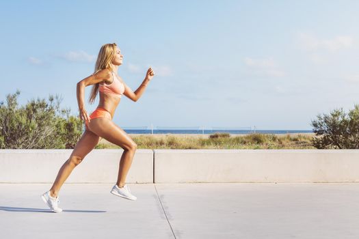 beautiful blonde female athlete running fast for the promenade, athletic sportswoman training, fitness and healthy lifestyle concept, dynamic movement, vertical photo with copy space for text