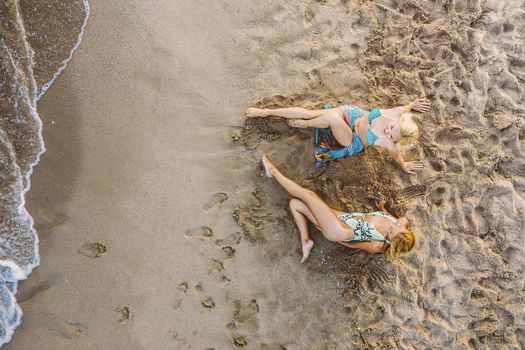 top view of two blond girls lying on the sand by the sea, concept of friendship and relaxation in the summer