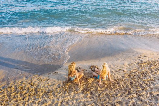 two blond women sitting on the shore of the beach, concept of friendship and relaxation in the summer