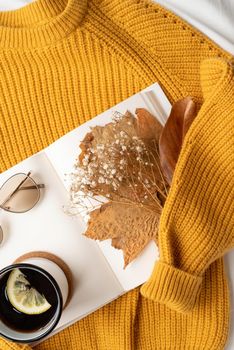 cozy composition of warm sweater, white book , cup of hot tea and autumn leaves , top view flat lay