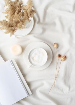 white blank book with cup of coffee and burning candle , cozy composition with opened book mockup on bed