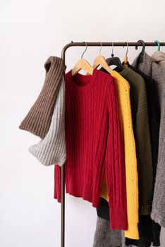 Row of different colorful Knitted sweaters hang on hangers, white background, autumn and winter season