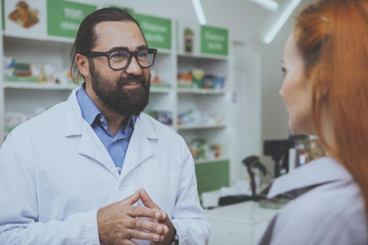 Friendly professional pharmacist talking to his female customer at the drugstore. Unrecognizable woman buying medicine at pharmacy. Service, healthcare, consumerism concept