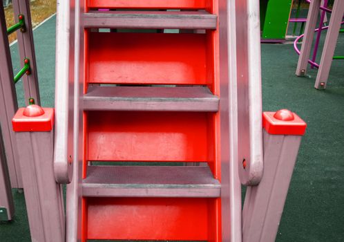 Close-up of wooden steps on an empty red staircase in an outdoor playground, a safe play area for children.