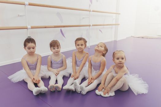 Cute little girls sitting on the floor, resting after ballet lesson at dance studio. Adorable little ballerinas wearing tutus relaxing together after exercising. Health, lifestyle, innocence concept