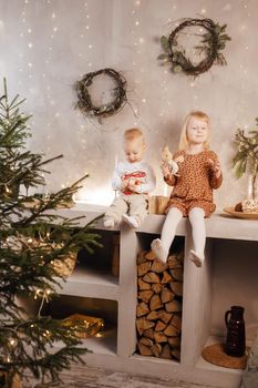 Little brother and sister play on Christmas eve in a beautiful house decorated for the New Year holidays. Children are playing with a Christmas gift. Scandinavian-style interior with live fir trees and a wooden staircase.