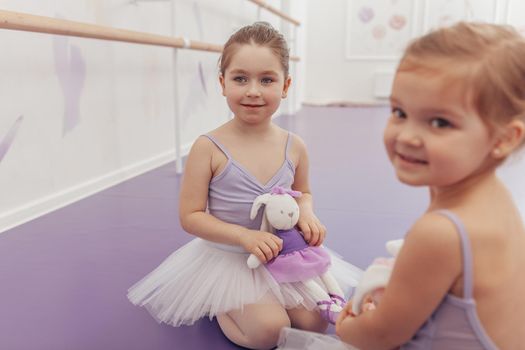 Cute little ballerinas sitting together at dance school before the lesson. Lovely little girl and her friend wearing tutus resting at ballet school after exercising