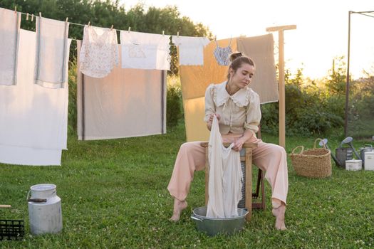 Laundry day. A woman hangs linen and towels on a tree in the courtyard of a village house. Summer cottage concept.