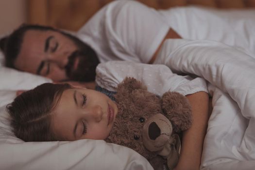 Adorable little girl hugging her teddy bear, sleeping in bed with her father. Cute little girl sleeping with her dad. Love, family, childhood concept