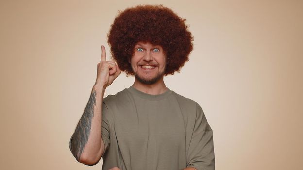 Eureka. Inspired man 30s in t-shirt pointing finger up with open mouth, showing Eureka gesture, solution, idea, inspiration, answer. Young adult guy isolated alone on beige studio wall background