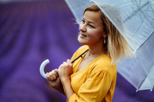 A middle-aged woman in a lavender field walks under an umbrella on a rainy day and enjoys aromatherapy. Aromatherapy concept, lavender oil, photo session in lavender.