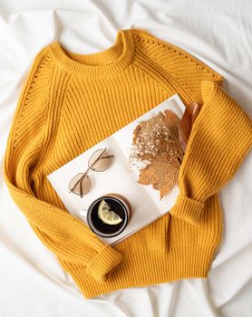 cozy composition of warm sweater, white book , cup of hot tea and autumn leaves , top view flat lay