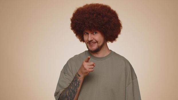 Hey you. Man 30s in t-shirt smiling excitedly and pointing to camera, choosing lucky lottery winner, indicating to awesome you. Young adult guy boy isolated alone on beige studio wall background