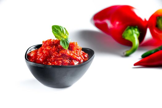 Red paste ajvar of red sweet peppers. on white background with ingredients for cooking