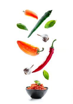 Ajvar in a black pial with basil on a white background. Isolate. Sweet bell pepper paste. ingredients fly in the air