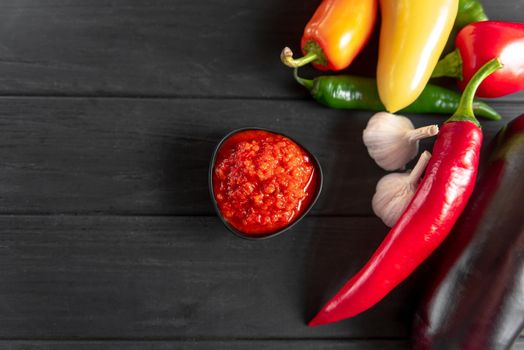 Ajvar in a black bowl with the ingredients red pepper chili peppers garlic on a wooden background. A classic Balkan dish