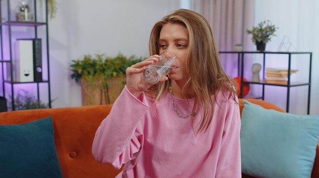 Portrait of thirsty lovely girl sitting indoors holding glass of natural aqua make sips drinking still water preventing dehydration. Woman with good life habits, healthy slimming, weight loss concept