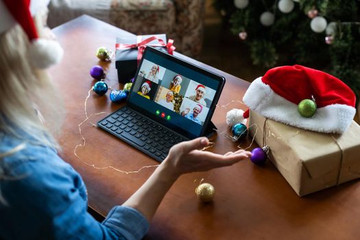 Christmas online holiday. Happy woman having video call with their family or friends. Young woman uses a digital tablet near decorated festive tree at home. Virtual meeting.