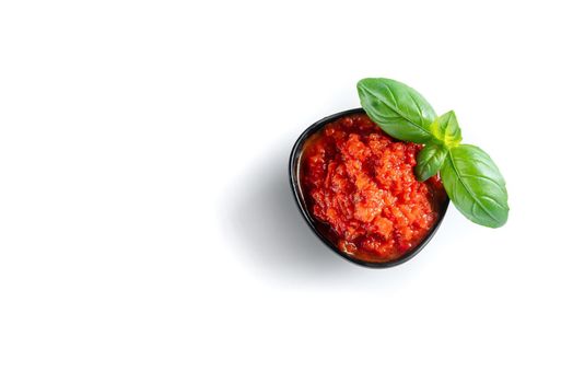 Ajvar in a black pial with basil on a white background. Isolate. Sweet bell pepper paste.