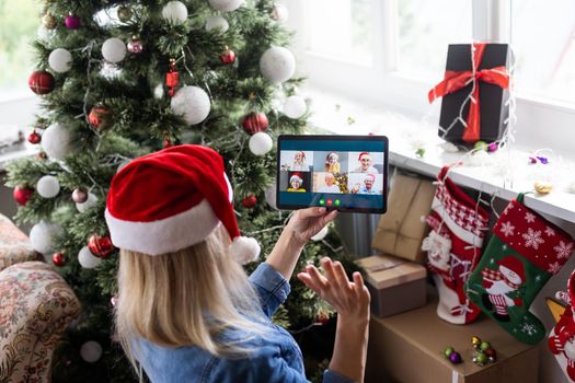 Christmas online holiday. Happy woman having video call with their family or friends. Young woman uses a digital tablet near decorated festive tree at home. Virtual meeting.