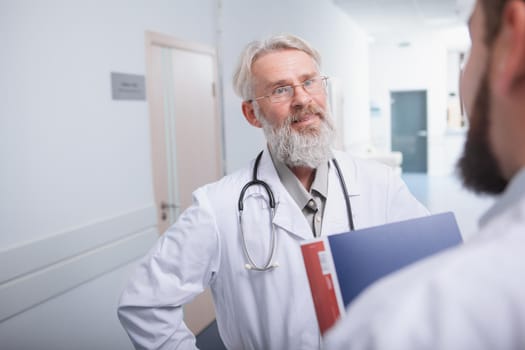 Senior male doctor smiling joyfully, talking to his assistant at the hospital. Medical workers chatting at the clinic