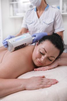 Vertical portrait of a happy plus size woman enjoying endospheres body treatment at beauty salon