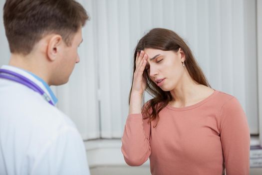 Young woman with fever or headache talking to the doctor. Sick female patient with migraine on medical appointment