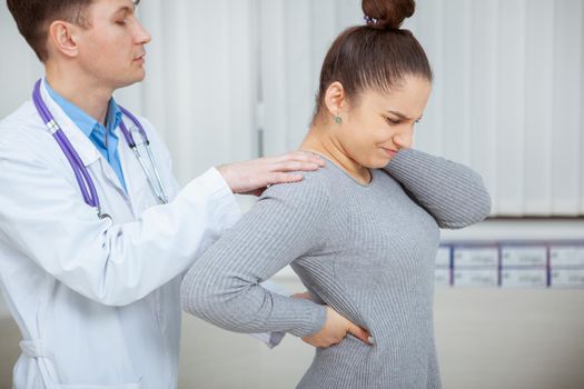 Young woman suffering from back pain, having her spine examined by experienced doctor