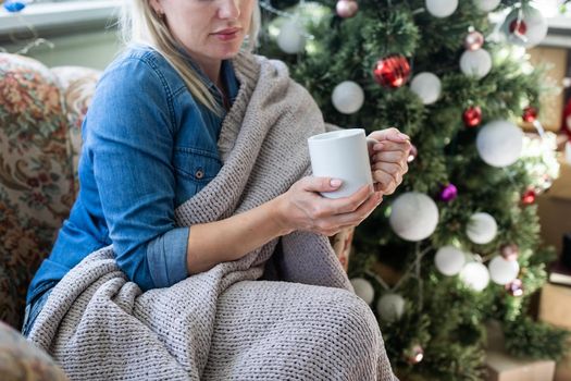 Young hispanic girl drinking coffee sitting on the sofa by christmas tree at home