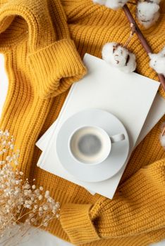 cozy composition of warm yellow sweater, white books , cup of hot coffee and dry flowers , top view flat lay