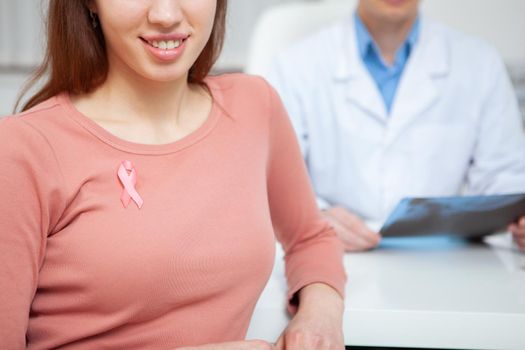 Cropped shot of a happy healthy woman with pink ribbon on her shirt. Female patient smiling supporting breast cancer awareness
