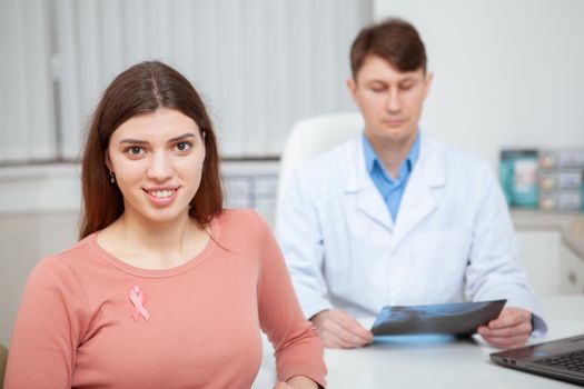 Beautiful young woman smiling to the camera, wearing breast cancer awareness symbol, pink ribbon on her shirt