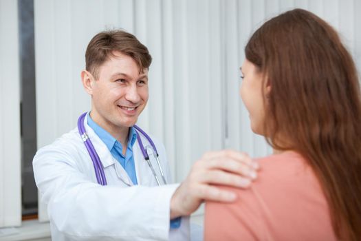 Cheerful male doctor smiling, comforting his female patient. Mature male practitioner cheering up young woman, helping her get healthier