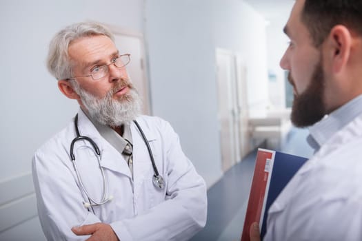 Elderly male doctor looking concerned, talking to his colleague at the clinic